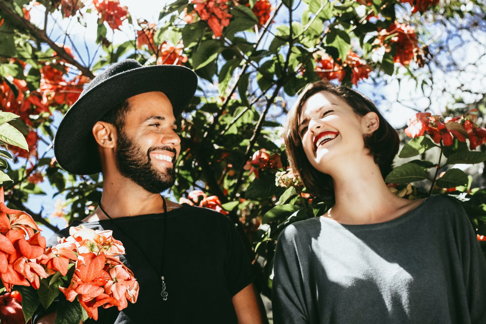 Homem e mulher sorrindo lado a lado em frente a uma árvore florida.