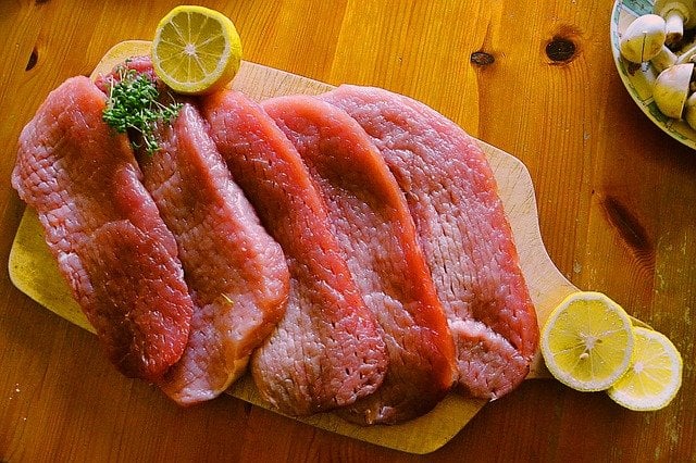 Peças de carne vermelha crua numa tábua com limões.
