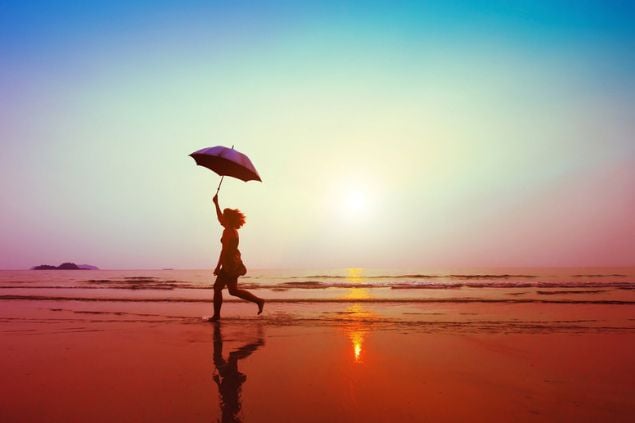 Mulher se protegendo com um guarda-chuva, na praia, mas de forma despretenciosa.