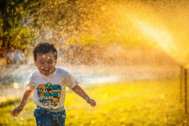 Menino correndo sorrindo com água espirrando no ar