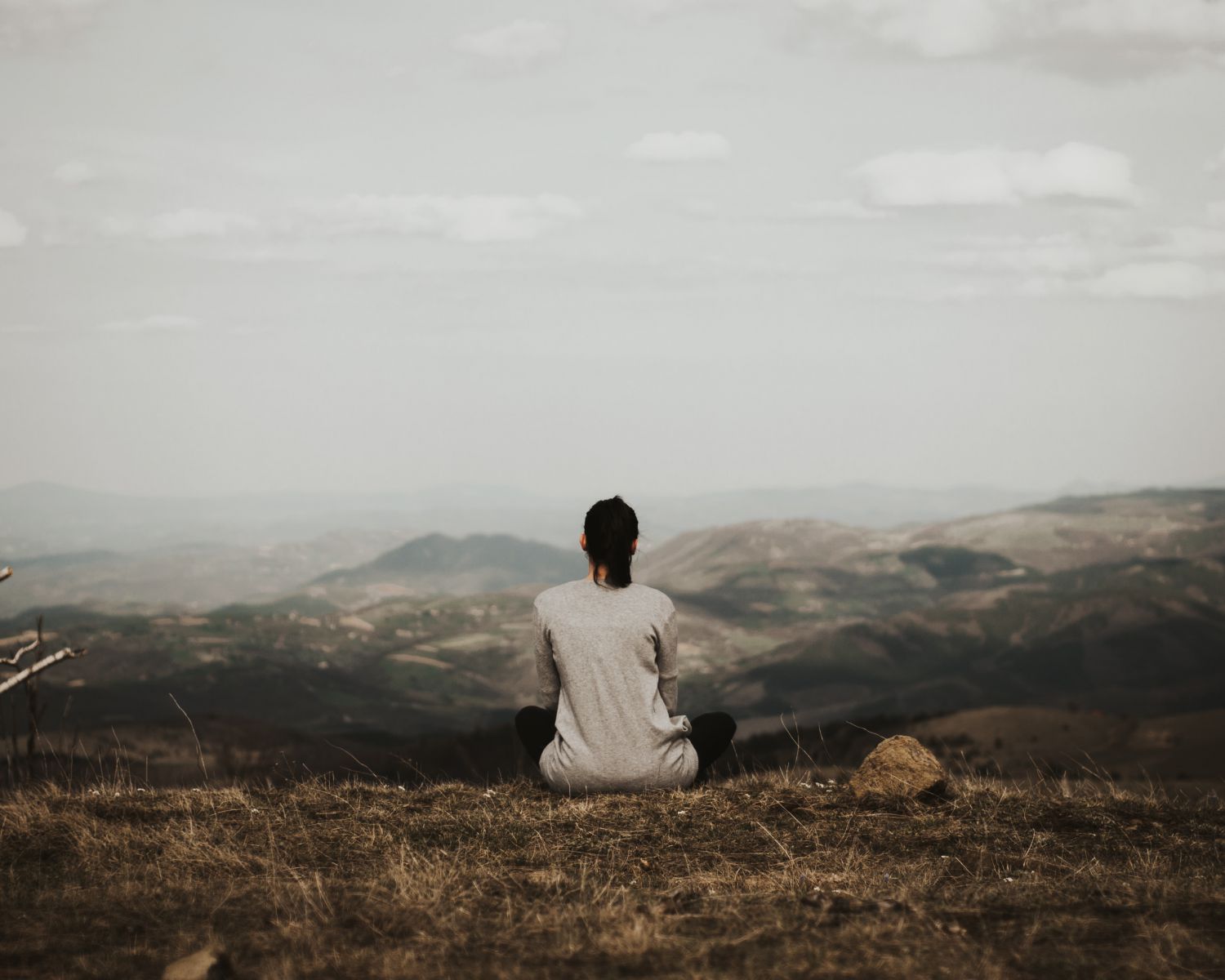 Mulher sentada no topo de uma montanha olhando para o horizonte