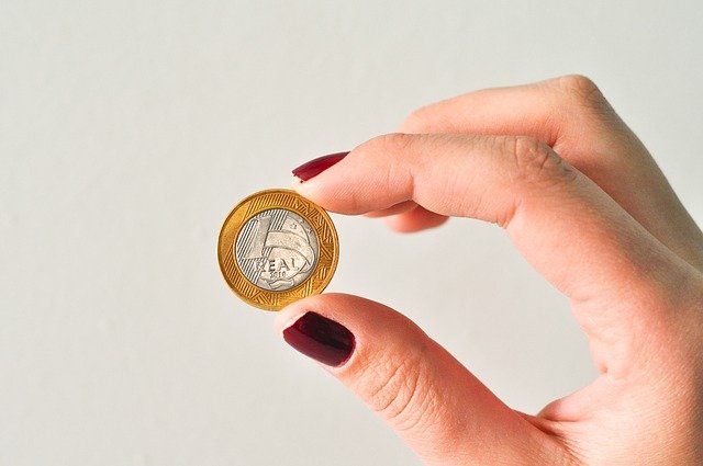 Mão branca feminina segurando moeda de um real.