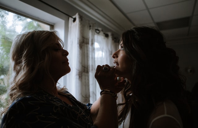 Omar Lopez / Unsplash Mulher branca passando batom em jovem branca.