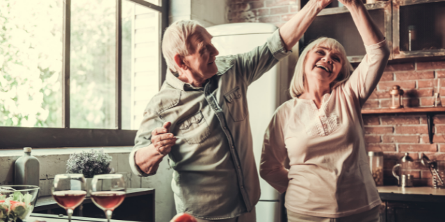 Um casal de idosos dança em uma cozinha.