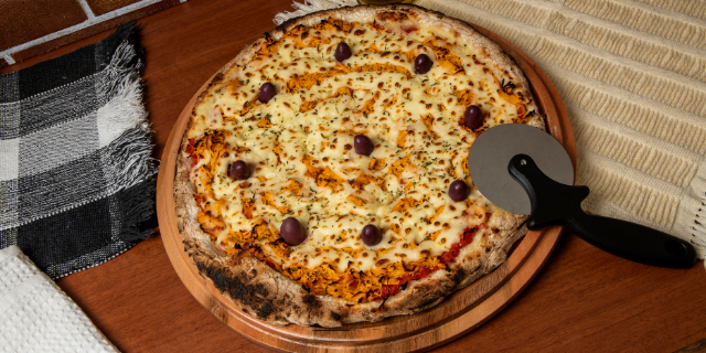 Pizza de frango e queijo. Sobre a pizza, há um cortador. 