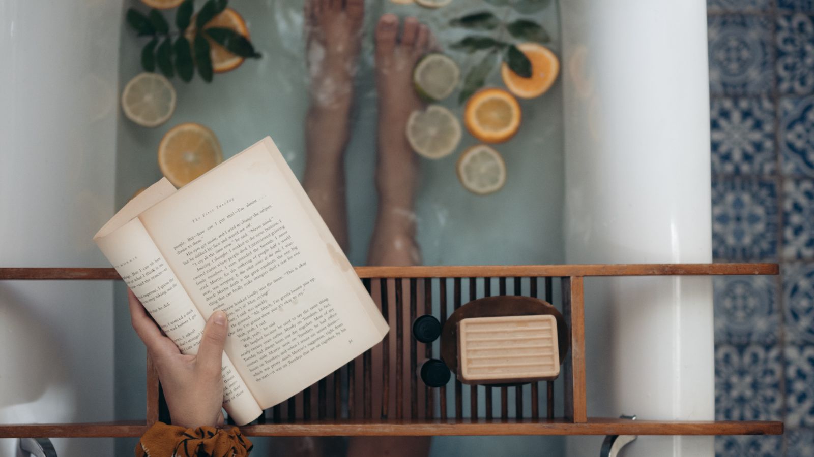 Pessoa sentada em uma banheira com rodelas de limão, lendo um livro.