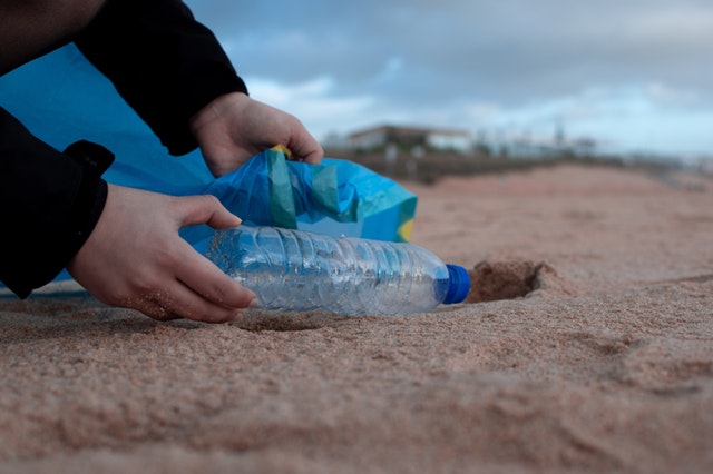 Voluntário recolhendo uma garrafa plástica da praia.