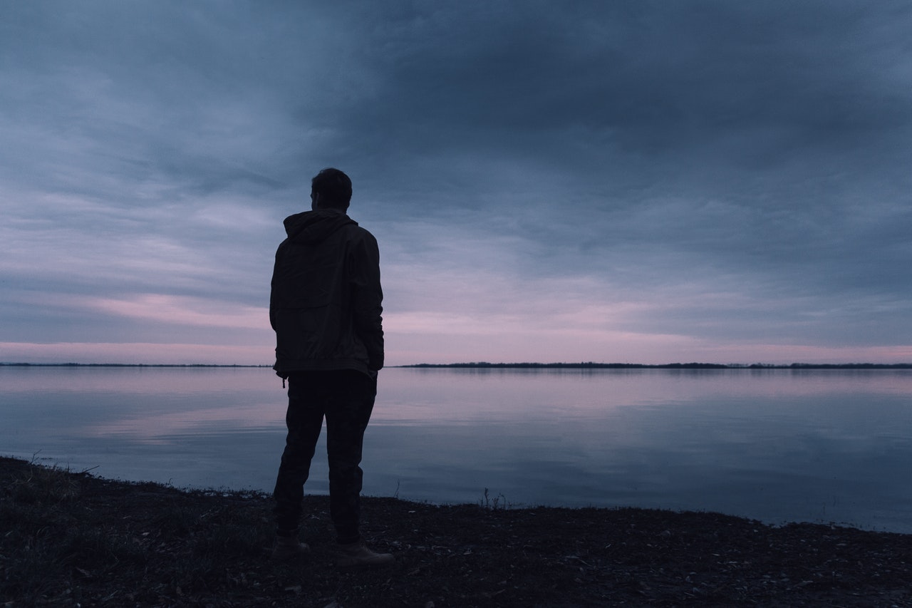 Homem de pé em frente a um lago em um dia nublado.