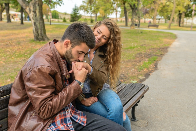 Homem beijando mão de mulher ambos sentados em banco de praça