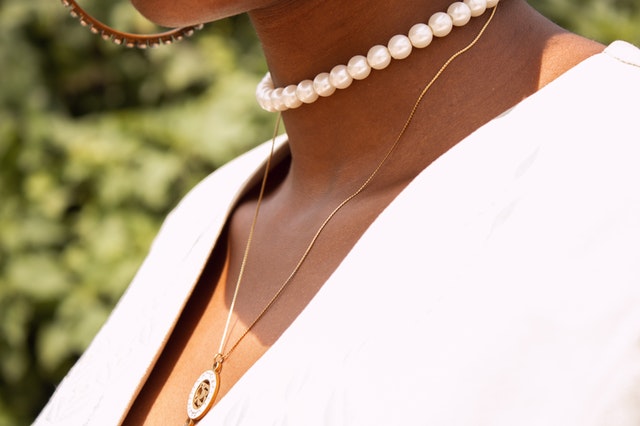 Pescoço de mulher negra com colares de pérolas e corrente com medalhão.