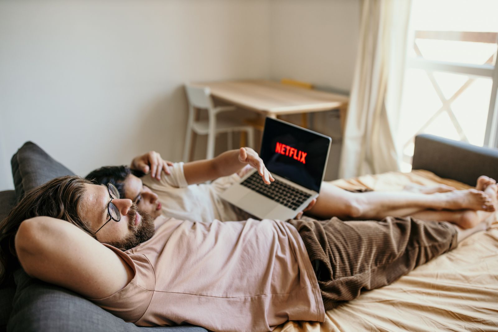 Homem e mulher brancos deitados abraçados numa cama com laptop no colo.