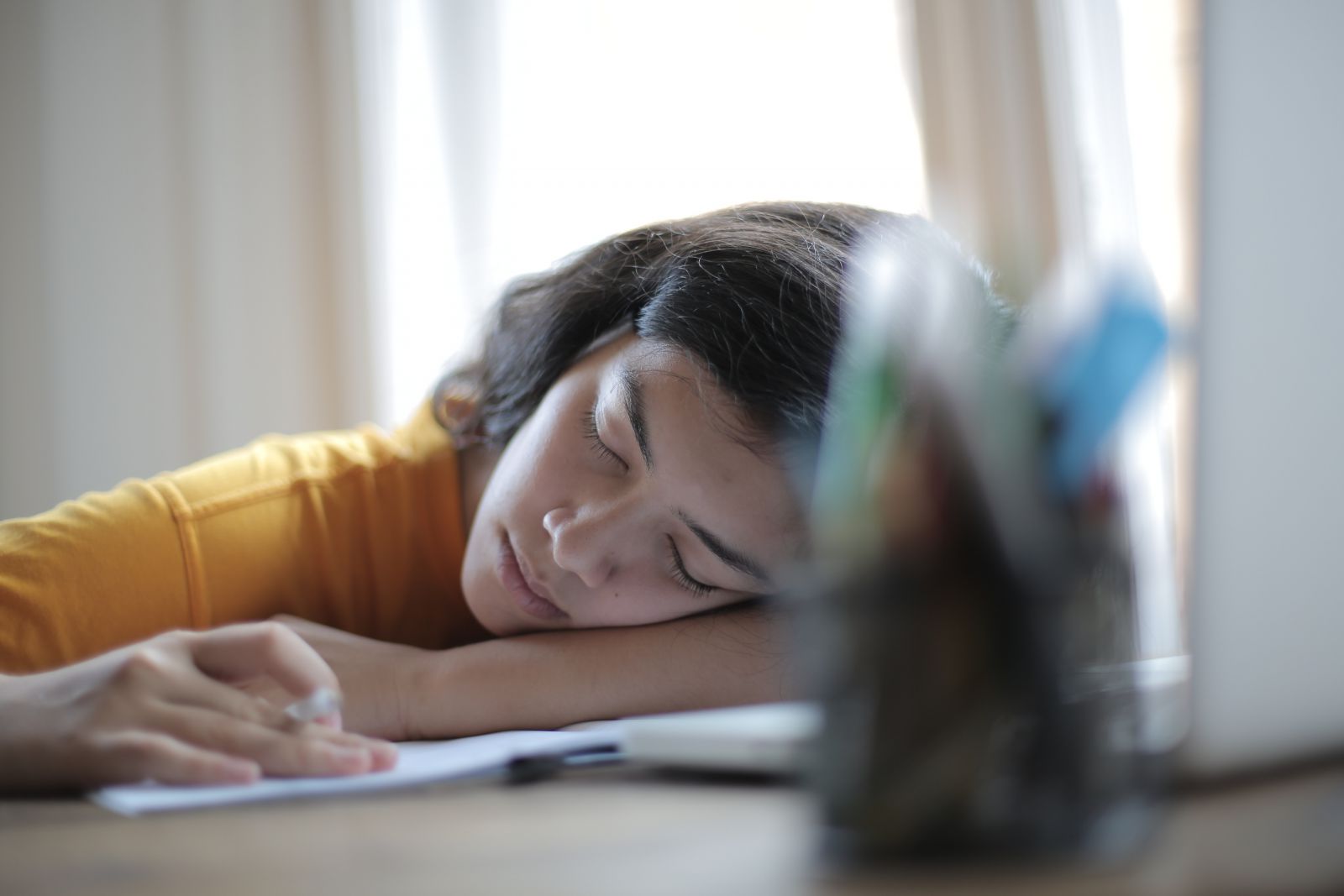 Mulher dormindo na mesa com caderno e notebook