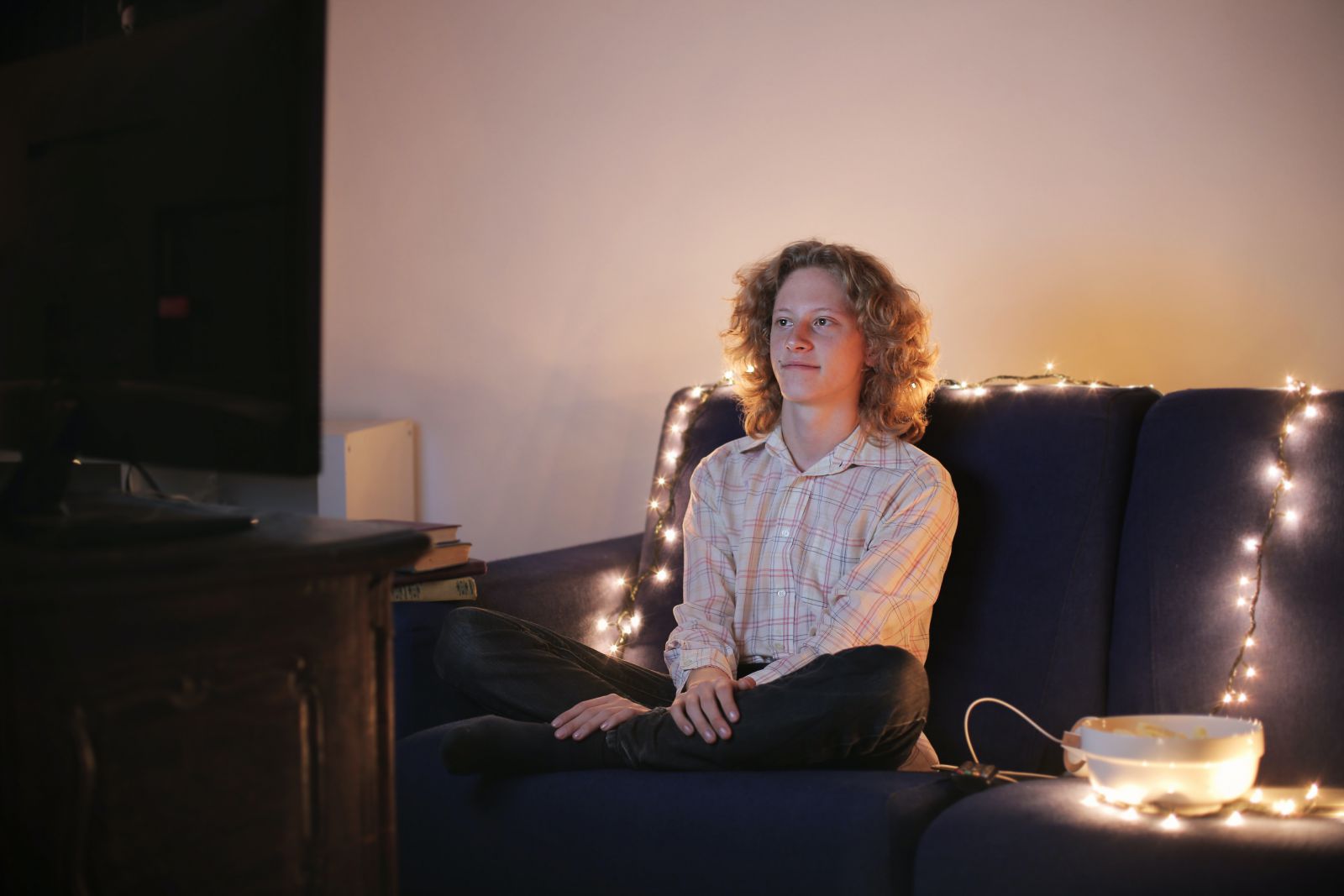 Jovem branco sentado de pernas cruzadas em frente à televisão.
