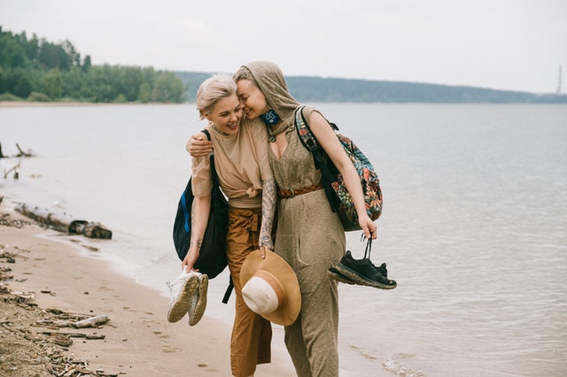 Duas mulheres brancas abraçadas de lado numa praia.