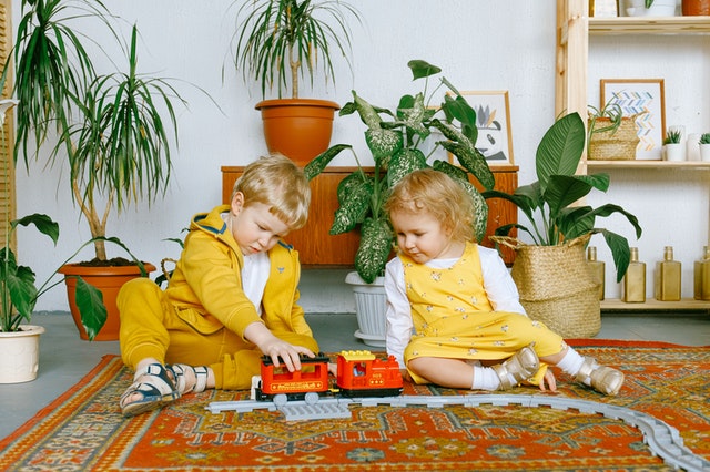 Irmão e irmã pequenos brincando com um trem de plástico no chão.