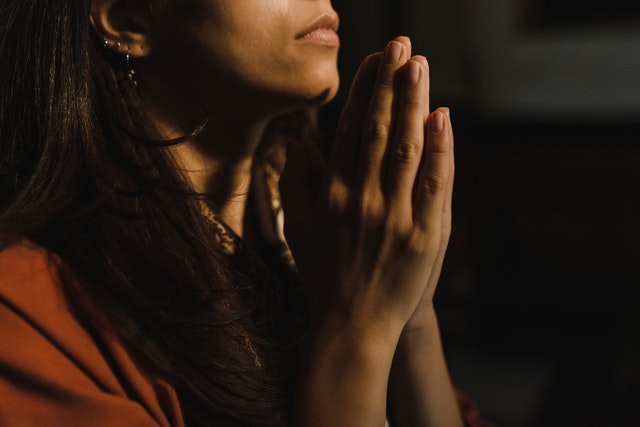 Mulher branca com as mãos juntas rezando.