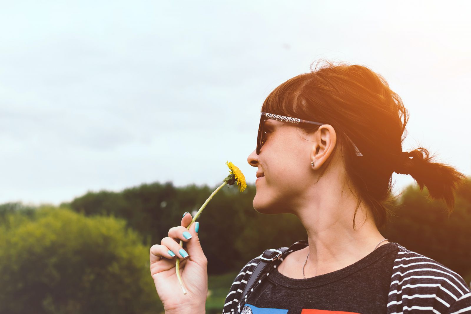 Mulher cheirando uma flor usando óculos de sol