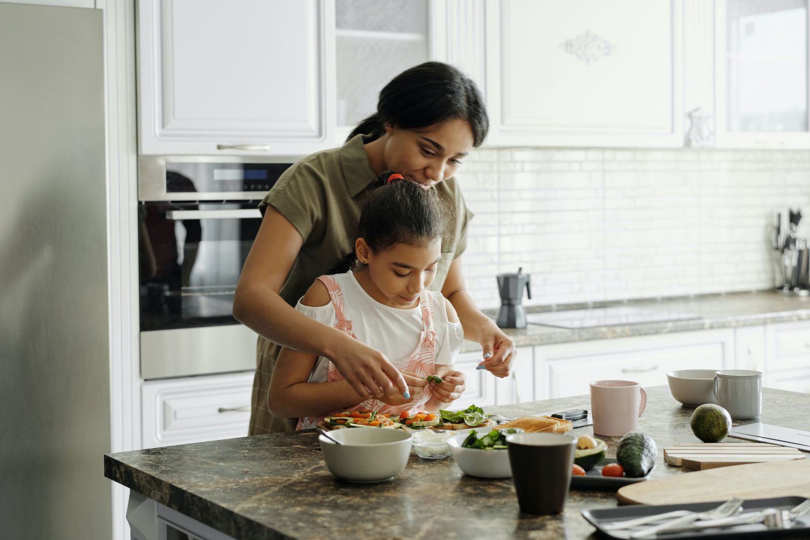 Mulher cozinhando com uma criança em frente a bancada da cozinha
