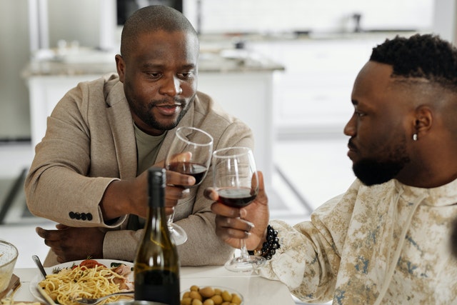 Dois homens brindando com taça de vinho em uma mesa com comida