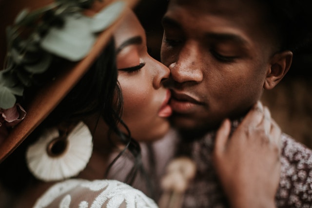 Homem e mulher com roupas sociais de olhos fechados, encostando seus lábios