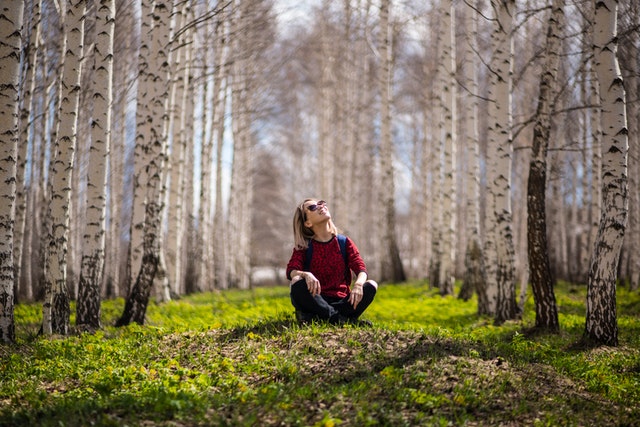 Garota sentada entre árvores olhando para o alto sorrindo
