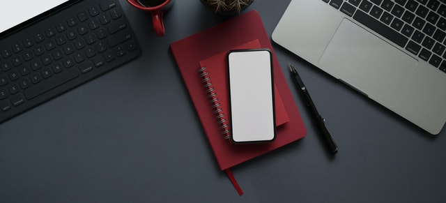 Mesa de trabalho com cadernos, notebook, celular e uma caneca.