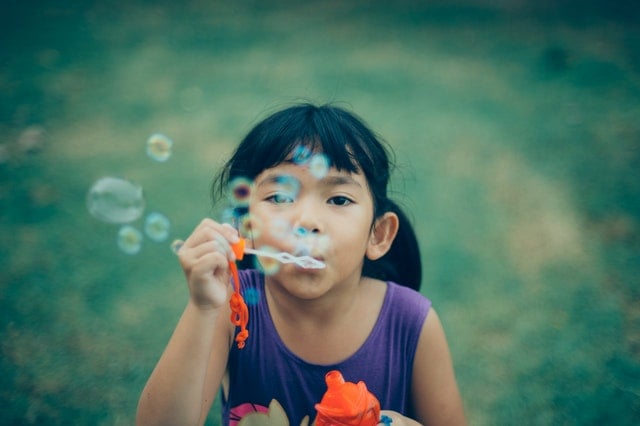 Menina com traços asiáticos soltando bolhas de sabão.