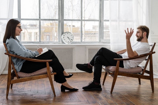 Homem e mulher brancos sentados em cadeiras durante uma terapia.