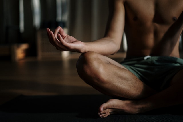 Homem sentado no chão com as pernas cruzadas, meditando