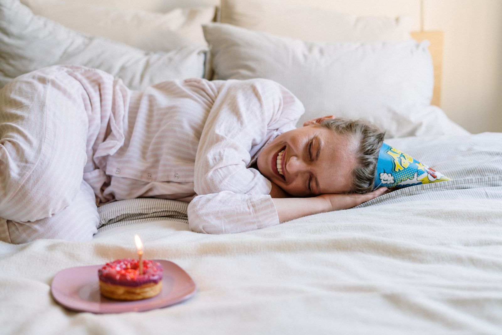 Mulher deitada na cama com bolo de aniversário a sua frente