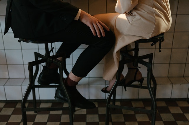 Mulher e homem sentados em bancos de um bar.