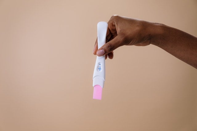 Mulher negra segurando teste de gravidez.