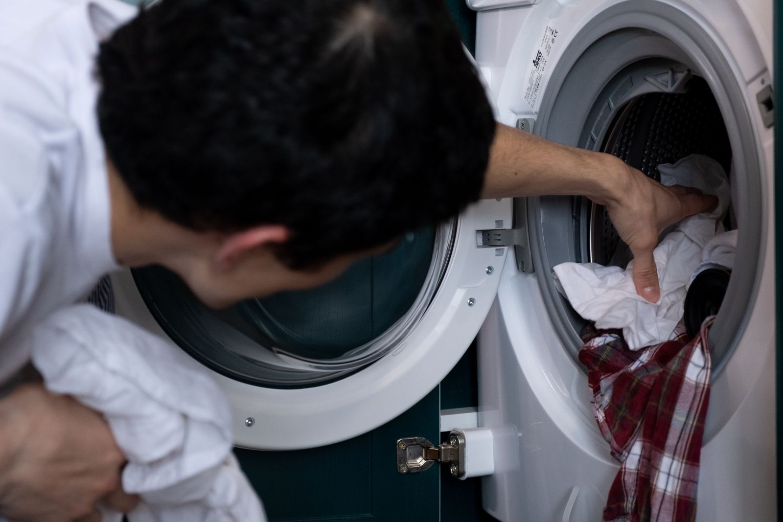 Homem colocando roupas na máquina de lavar