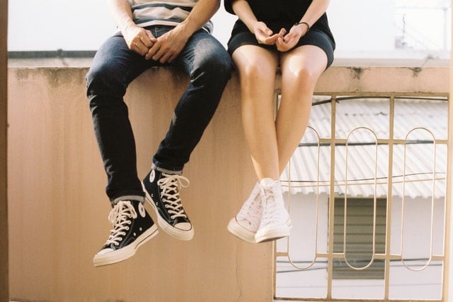 Dois pares de pernas brancas, um masculino e um feminino, sentados num muro