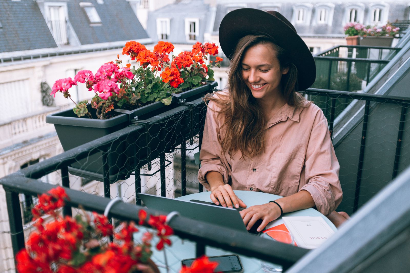 Mulher sorrindo enquanto trabalha com seu computador na varanda ao lado de vasos de flores