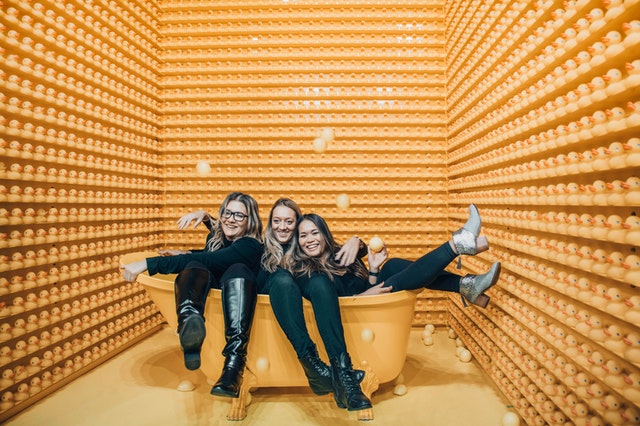 Três mulheres brancas e loiras dentro de uma banheira amarela.