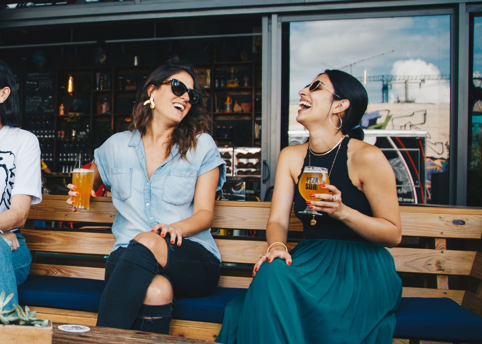 Duas mulheres sentadas em uma cadeira segurando copo de cerveja