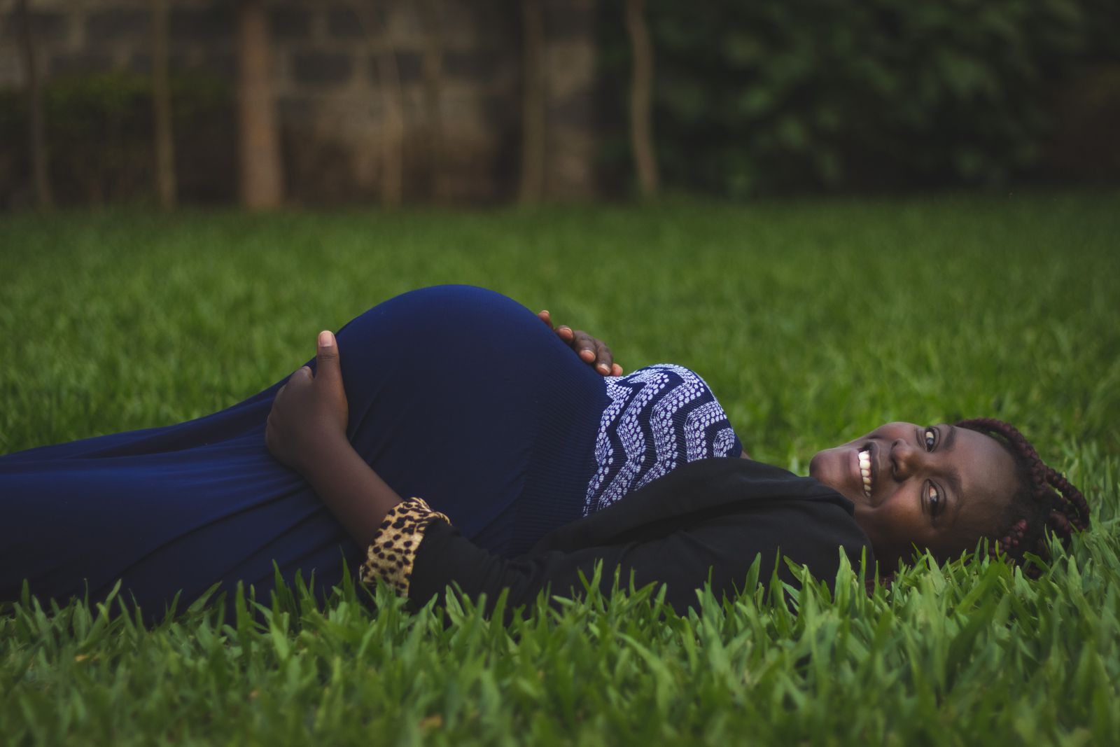 Mulher grávida deitada no gramado e sorrindo
