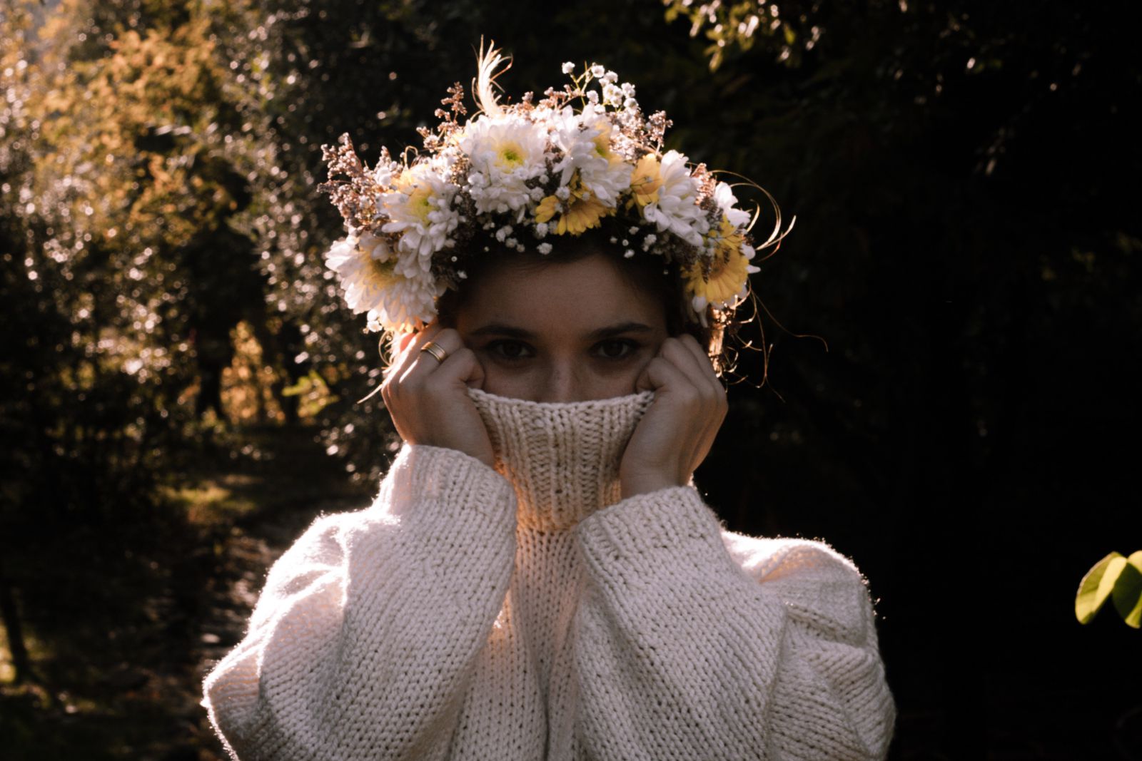 Mulher com flores na cabeça cobrindo seu rosto com sua blusa