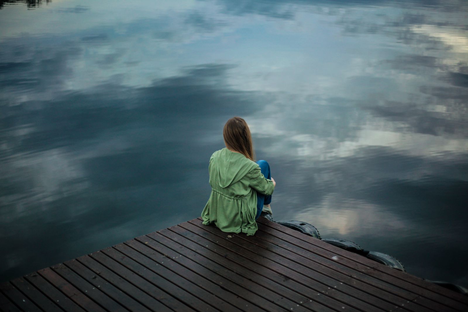Mulher sentada de frente para um lago