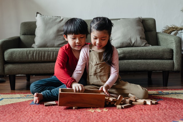 Irmão e irmã sentados no chão abrindo um jogo de peças de madeira.