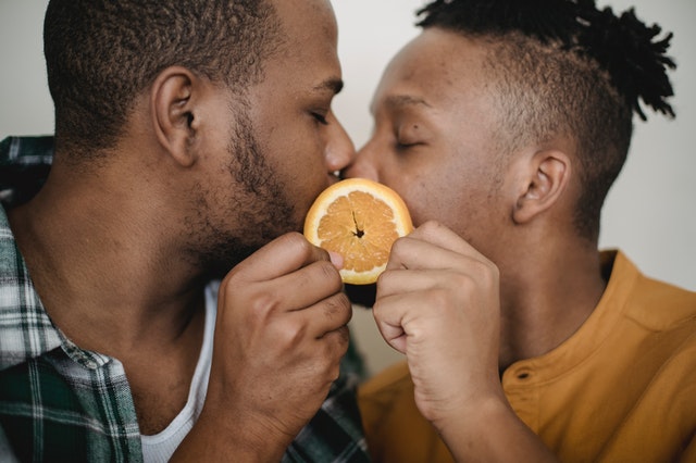 Homens negros se beijando segurando rodela de laranja.