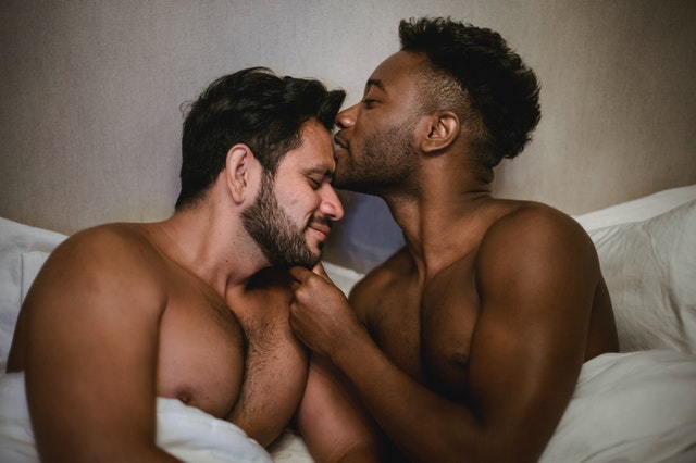 Homens negro e branco juntos numa cama.