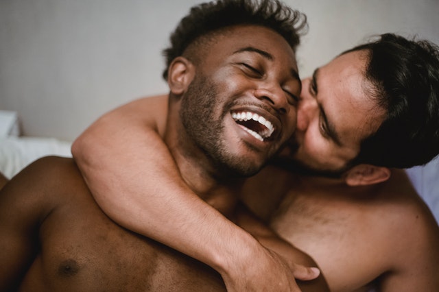 Homem branco abraçando e beijando bochecha de homem negro.