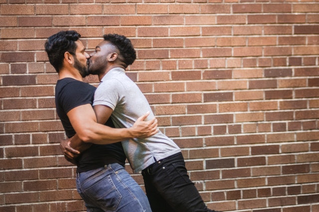 Homem negro e homem branco se beijando.