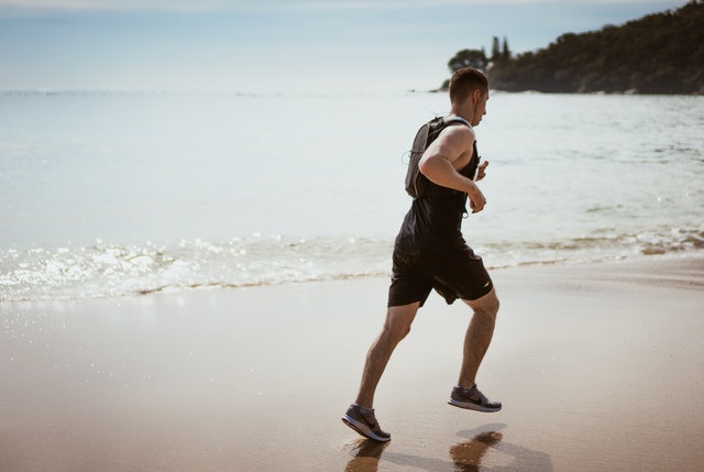 Homem branco correndo na praia.