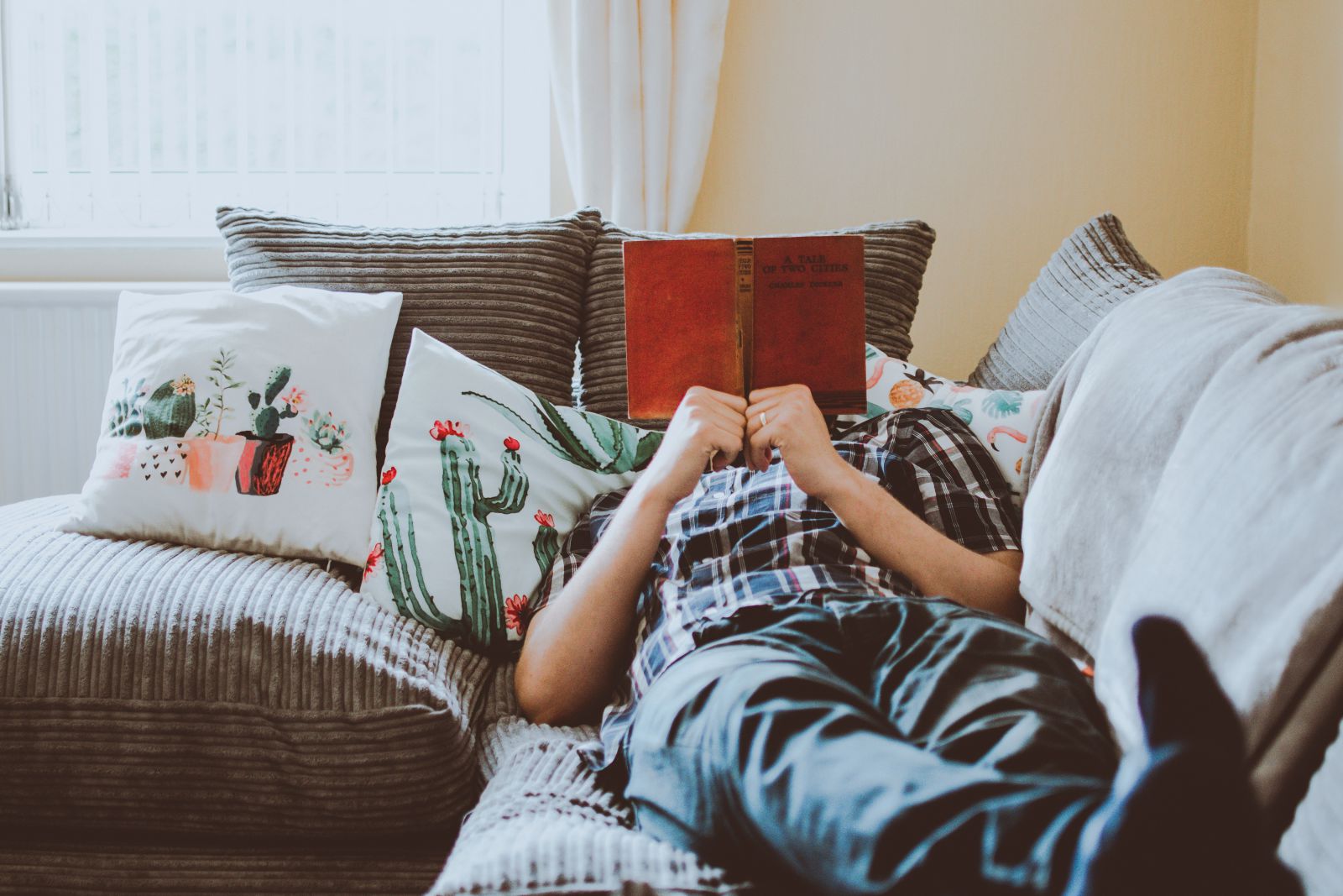 Pessoa deitada no sofá da sala lendo um livro