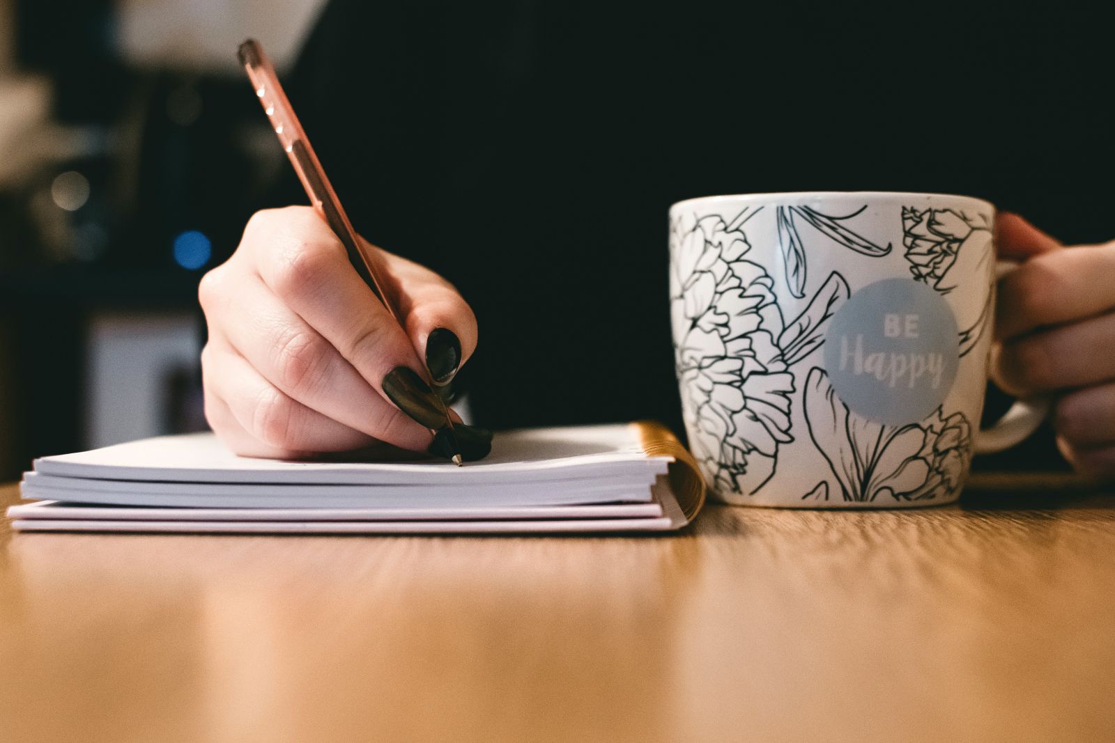 Mulher escrevendo em um caderno e segurando uma xícara