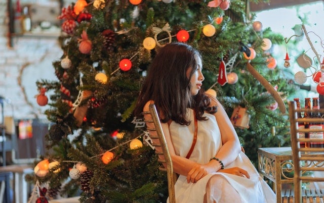 Menina sentada em uma cadeira de lado para uma árvore de Natal