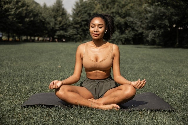 Mulher negra meditando ao ar livre.